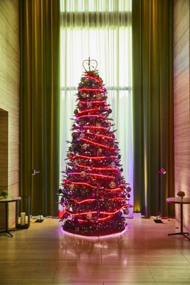Elegant Christmas tree with red lights and ornaments in a modern room with tall curtains and minimalistic decor.