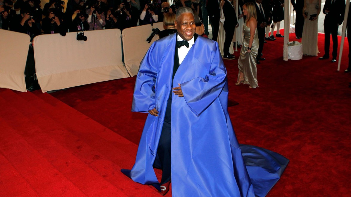 Person in blue robe walking red carpet with photographers in the background.
