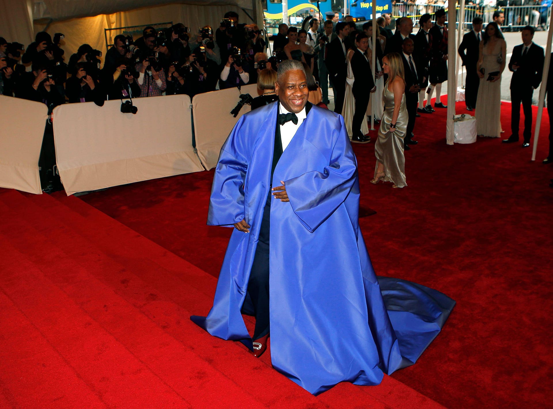 Person in blue robe walking red carpet with photographers in the background.
