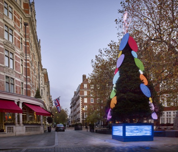 Decorated Christmas tree on a city street with surrounding buildings and a British flag in the background.
