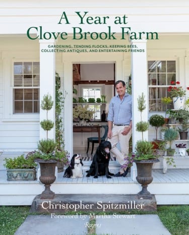 Person with two dogs on a porch surrounded by plants, cover of "A Year at Clove Brook Farm" book.