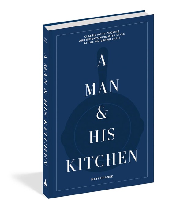 Blue cookbook titled "A Man & His Kitchen" by Matt Hranek, featuring a stylized pan on the cover.