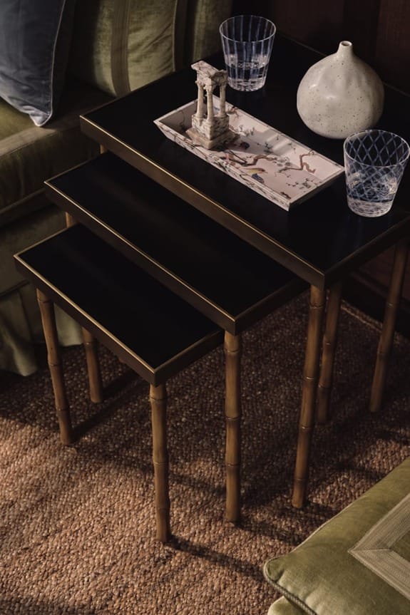 Stacked black coffee tables with gold trim, adorned with decorative items and glasses, set on a woven rug in a cozy room.
