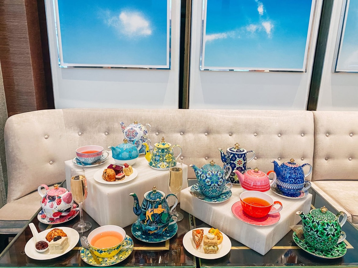 Colorful tea set with patterned teapots, cups, and saucers displayed on a table, accompanied by desserts and champagne glasses.