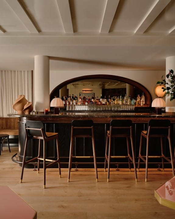 Elegant bar interior with high stools, curved counter, and a variety of bottles displayed against a mirror backdrop.