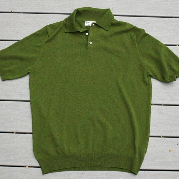 Green short-sleeve polo shirt laid flat on gray wooden surface.