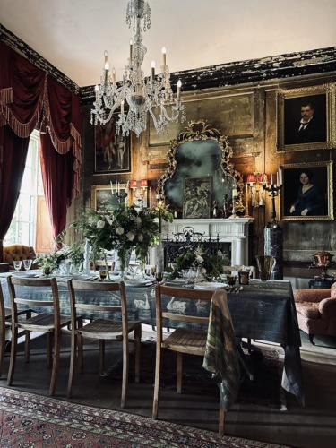 Elegant vintage dining room with ornate chandelier, large framed paintings, and a table set for a formal gathering.
