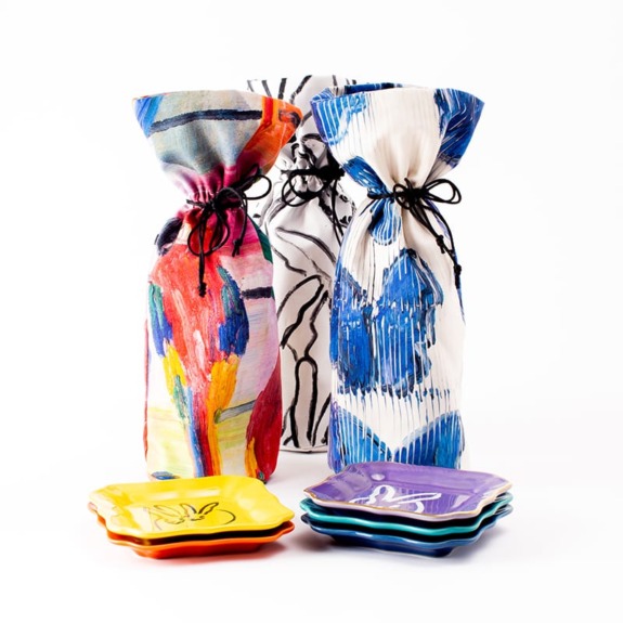 Colorful wrapped bottles with abstract patterns next to stacked multicolored plates on a white background.