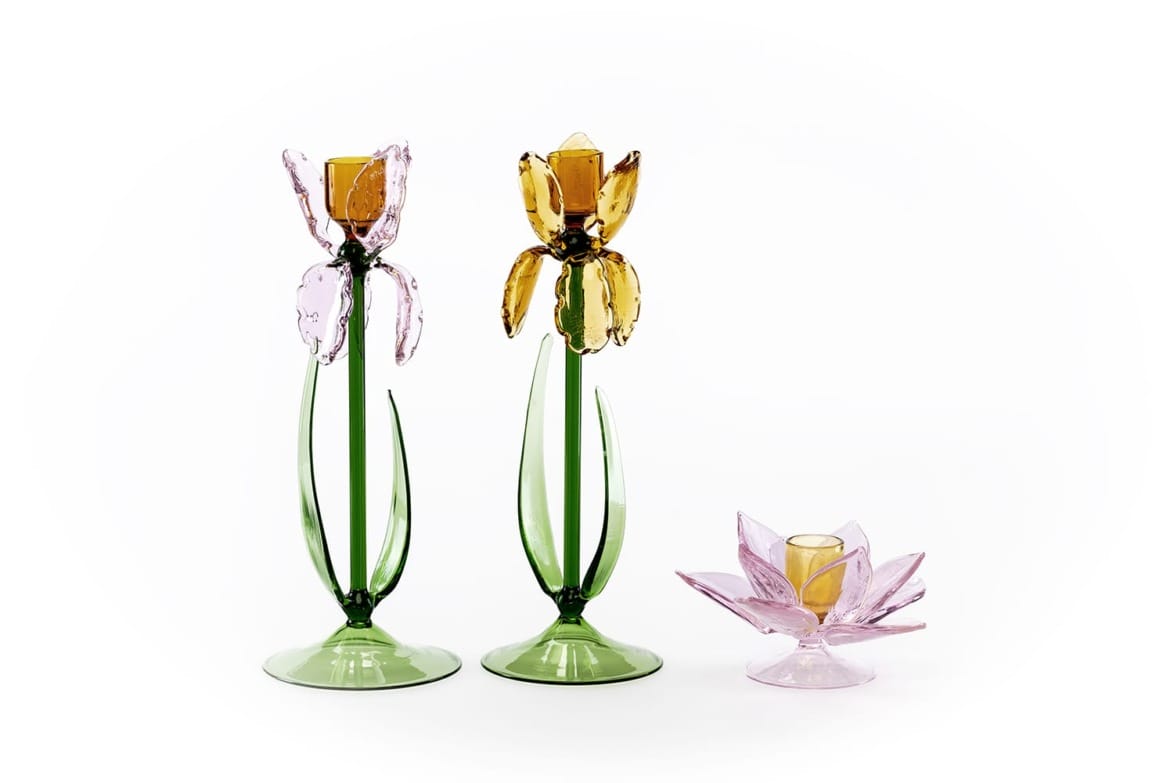 Three floral-shaped glass candle holders, two tall with yellow petals and one small pink, on a white background.