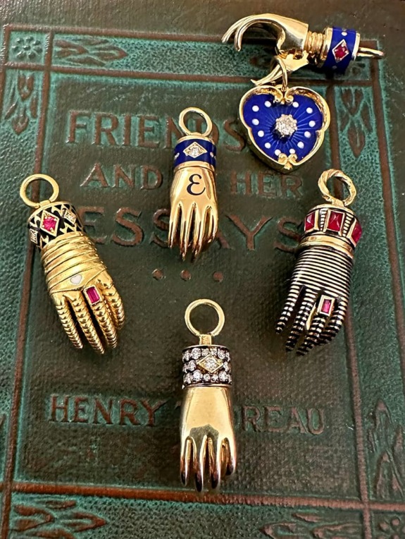 Gold hand-shaped charms with various gemstone designs and a heart charm on a book cover.