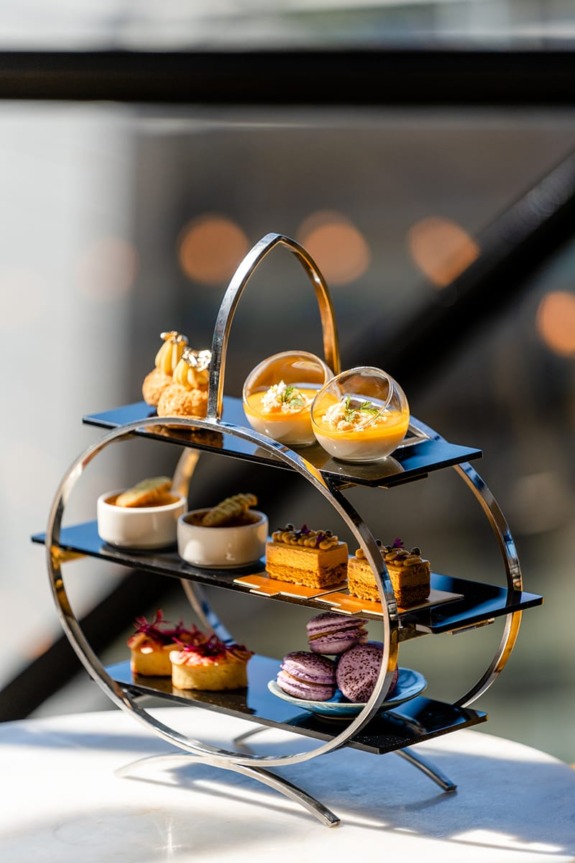 Elegant three-tiered stand displaying assorted pastries and desserts on a white table with a blurred background.