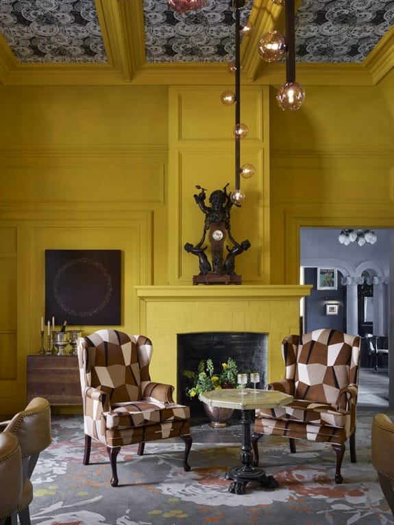 Yellow room with patterned chairs, a central yellow fireplace, floral ceiling, and pendant lights.
