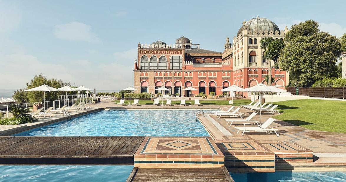 Outdoor pool with lounge chairs, surrounded by a historic building with domes and a sign reading "Restaurant" in the background.