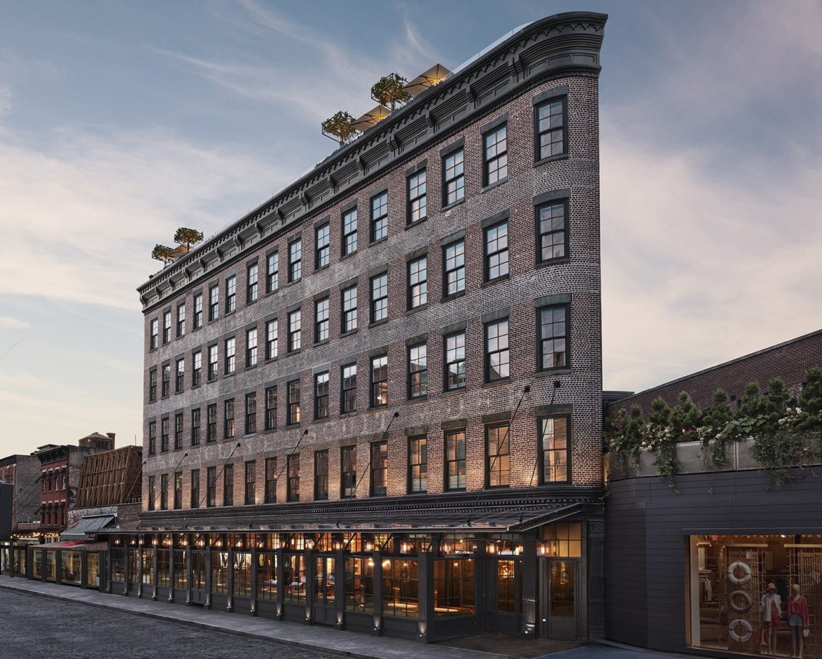 Historic multi-story brick building with large windows and decorative rooftop elements under a cloudy sky at dusk.