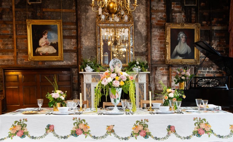 Elegant dining table with floral centerpiece, candles, and ornate decor in a vintage room with portraits on the walls.