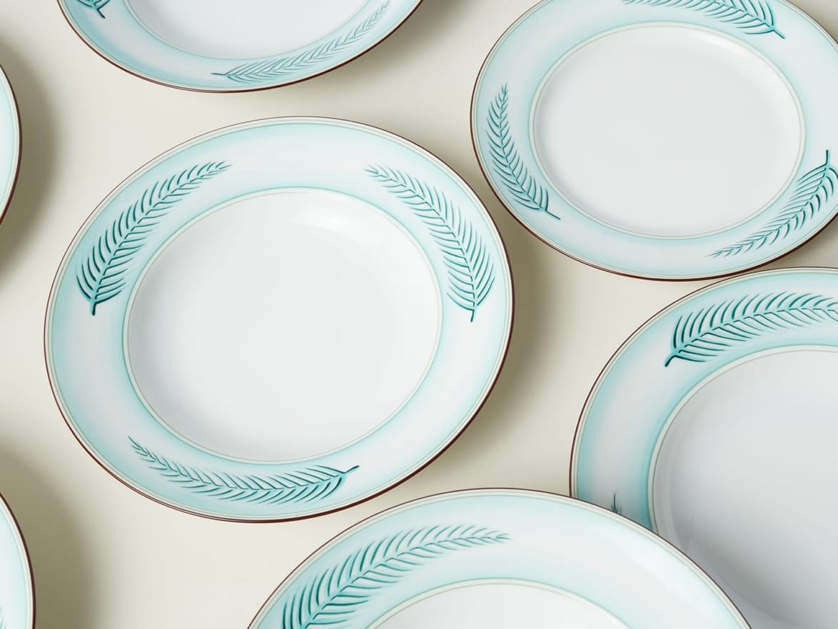Several white ceramic plates with green leaf patterns arranged on a white background.