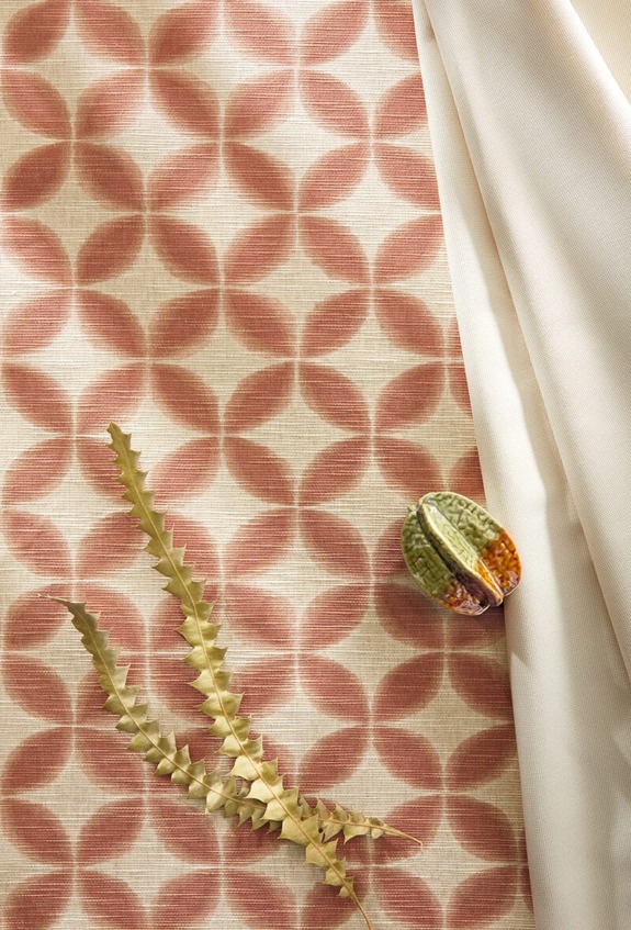 Geometric pink patterned fabric with a small plant and beige drape arranged beside a colorful seed pod.