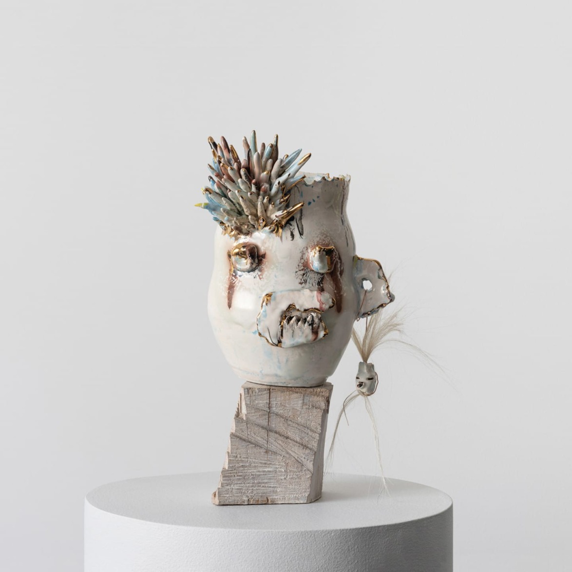 Ceramic sculpture with cactus-like features and eyes on a white pedestal against a plain background.
