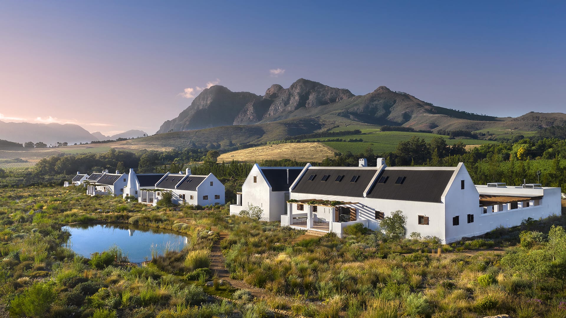 Scenic view of white buildings surrounded by lush greenery with mountains in the background under a clear blue sky.