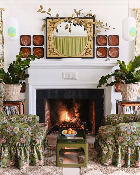 Cozy living room with floral armchairs, a lit fireplace, and a decorative mirror above the mantel.