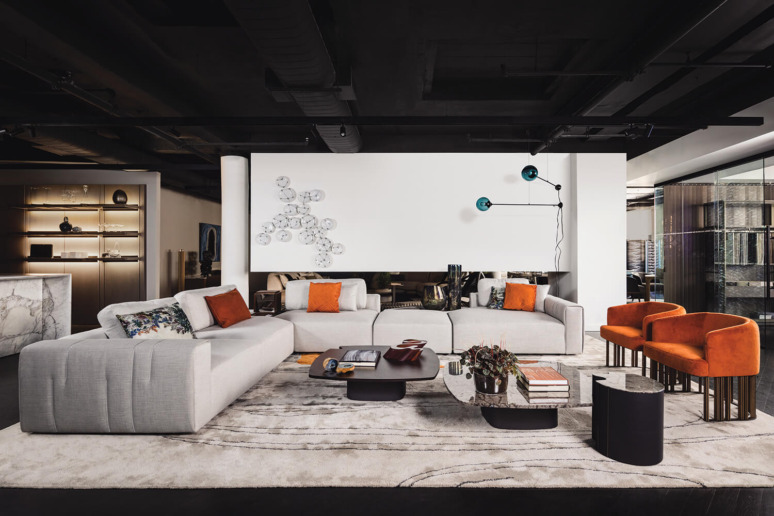 Modern living room with sleek white sofas, orange cushions, abstract wall art, and a contemporary coffee table on a patterned rug.