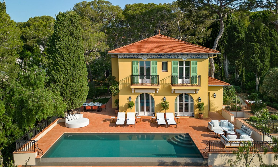 Mediterranean-style villa with pool, sun loungers, and outdoor seating surrounded by lush trees and greenery.