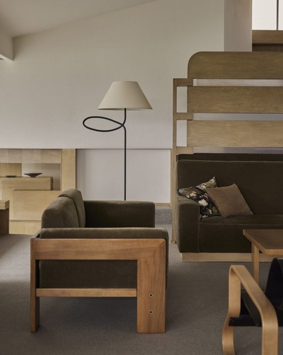 Modern living room with wooden furniture, olive green sofas, a floor lamp, and a decorative pillow on one sofa.