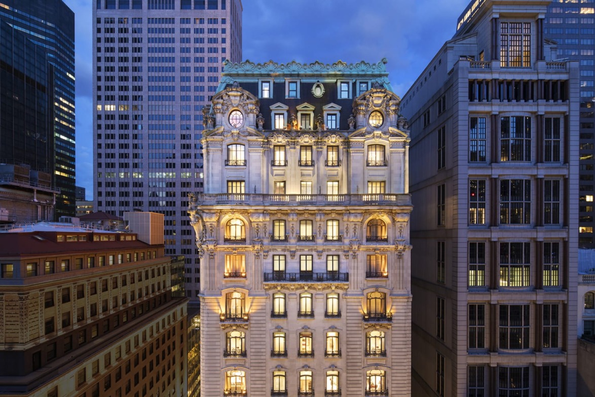 Illuminated historic building at dusk in a cityscape with surrounding skyscrapers, showcasing intricate architectural details.