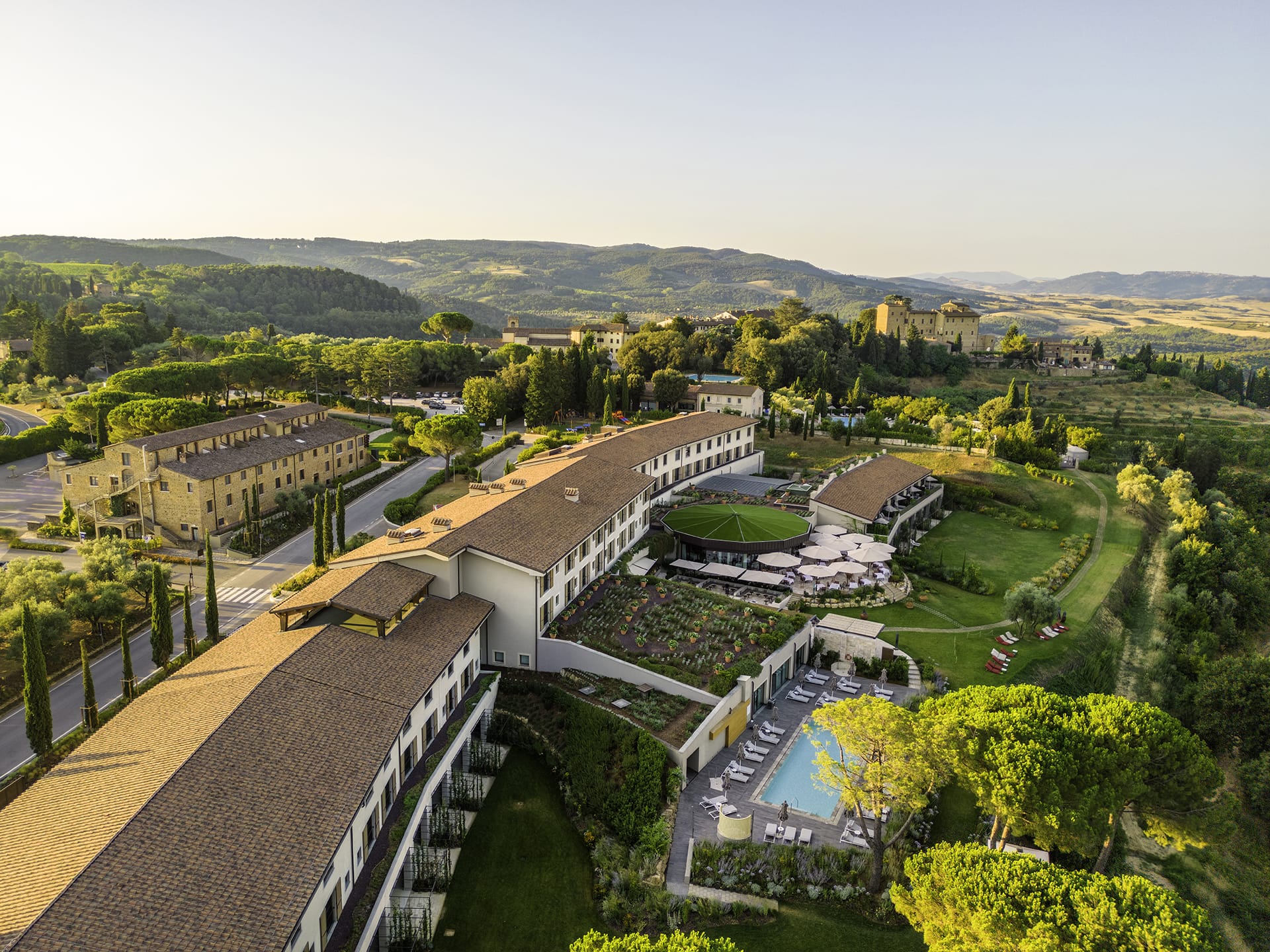 Aerial view of scenic countryside resort with pool, surrounded by trees, rolling hills, and distant mountains at sunset.