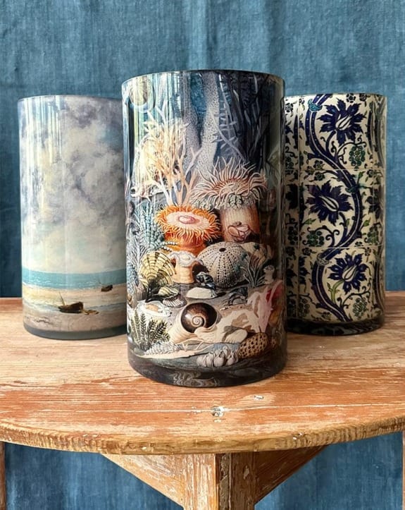 Three decorative cylindrical vases with ocean, marine life, and floral patterns displayed on a wooden table.