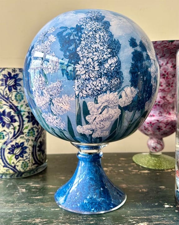 Glass sphere on a pedestal featuring intricate floral designs in blue and white, displayed on a wooden surface.