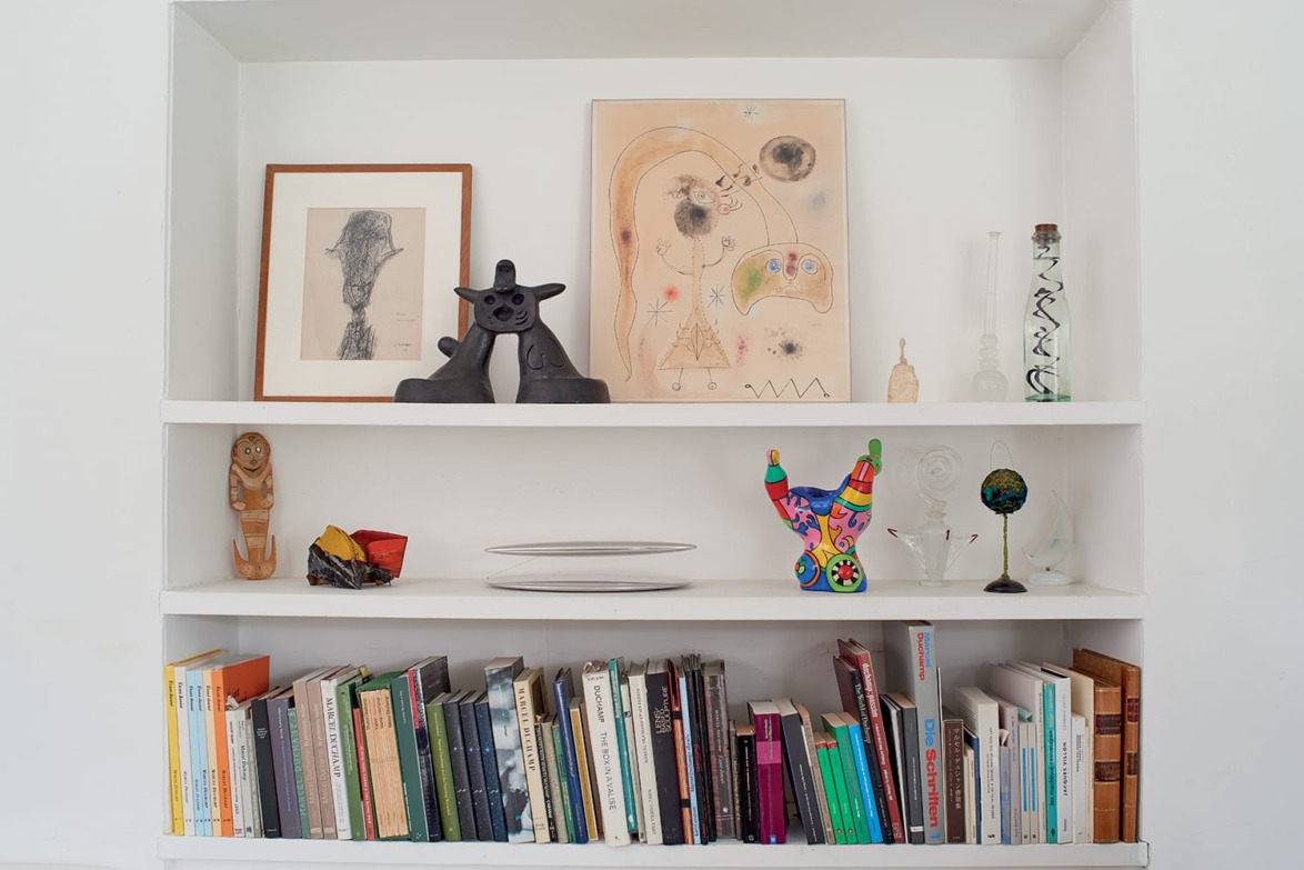 Bookshelf with books, eclectic art pieces, colorful sculptures, and framed artwork decorating the shelves.