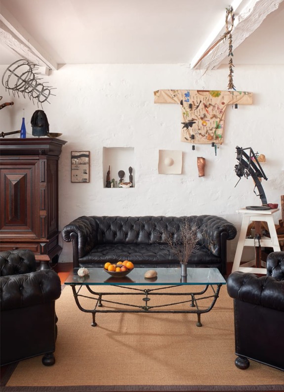 Eclectic living room with black leather sofas, glass coffee table, wall art, and unique sculptures on a beige rug.