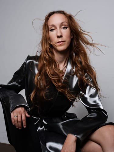 Iris van Herpen poses against a gray backdrop.