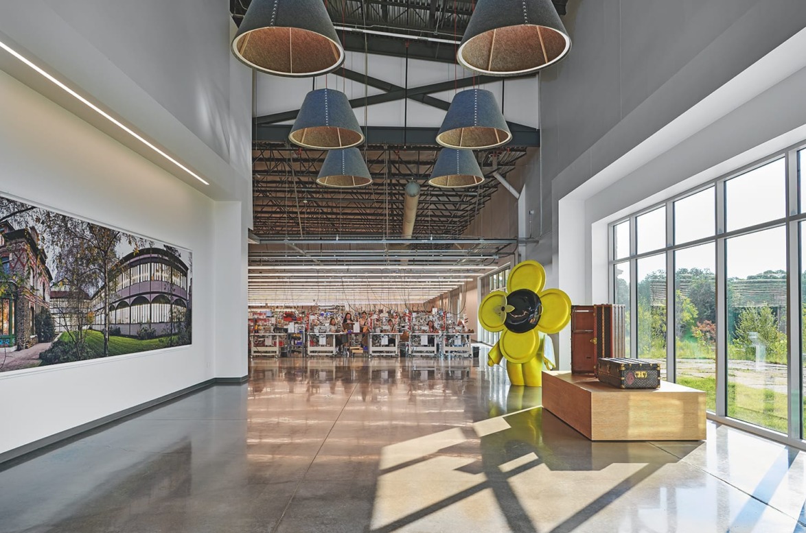 Modern art gallery interior with large yellow flower sculpture, high ceilings, hanging lights, and artwork on the wall.