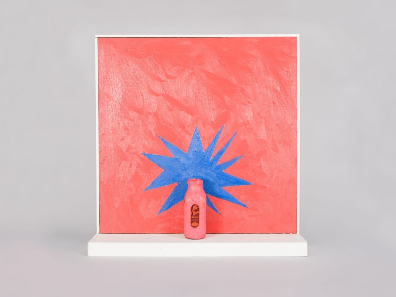 Pink bottle in front of a red canvas with a blue starburst design on a white shelf.