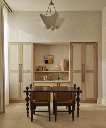 Elegant dining area with wooden cabinets, modern chandelier, dark wood table, and two leather chairs in a neutral-toned room.