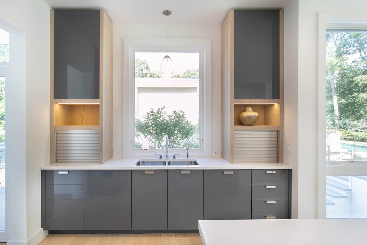 Modern kitchen with sleek gray cabinets, a large window, and a central sink illuminated by a pendant light.