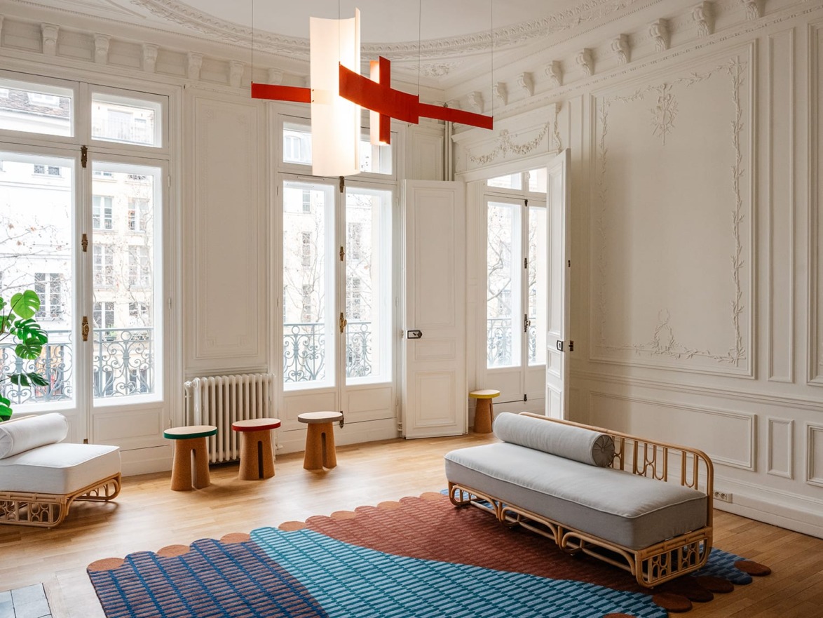 Elegant living room with ornate molding, modern furniture, colorful rug, red pendant light, and large windows with natural light.