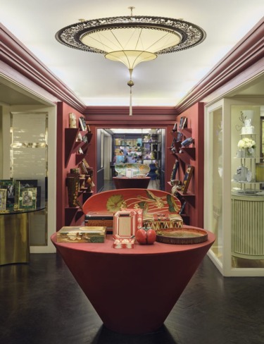 Elegant interior of a luxury store with decorative items on display tables and shelves, under an ornate chandelier.