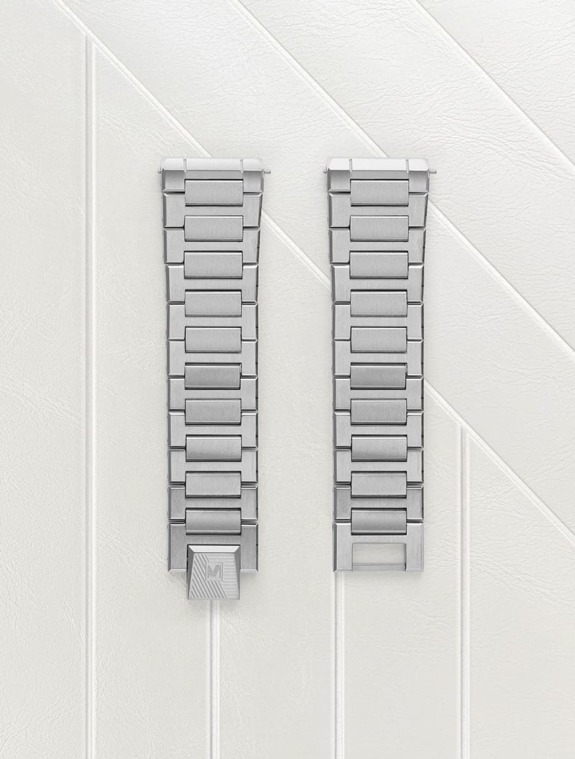 Silver metal watch bands on a light textured background, displayed side by side, with sleek, modern styling.