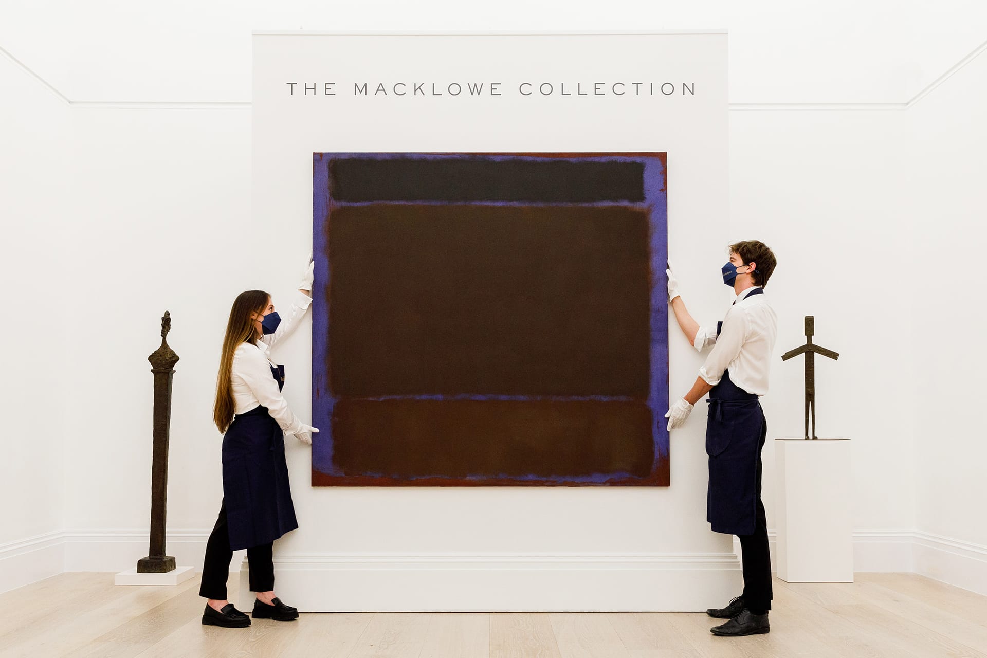 Two museum staff members display a large abstract painting from The Macklowe Collection.