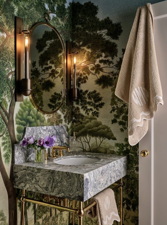 Elegant bathroom with nature-themed wallpaper, marble sink, and round mirror, featuring rustic lighting and beige towels.