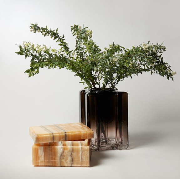Smoky glass vase with green foliage beside two stacked onyx boxes on a light background.