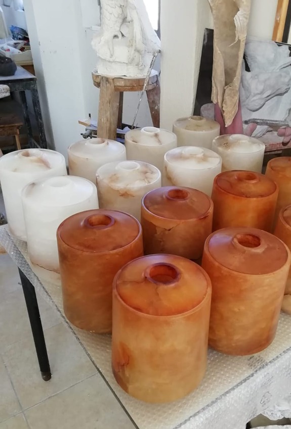 Several cylindrical stone art pieces, predominantly in shades of white and orange, displayed on a table in a workshop.