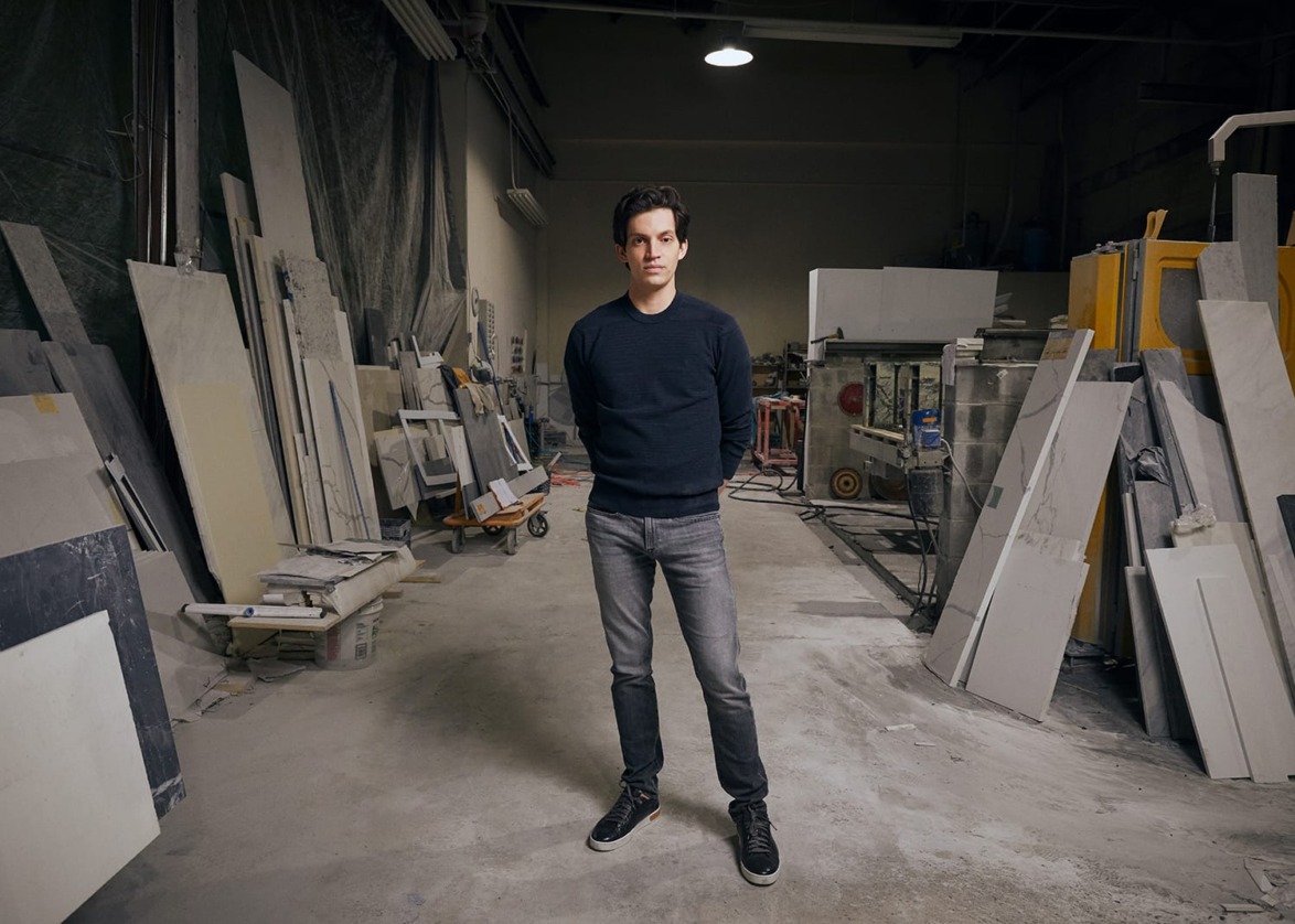 Person standing in a workshop surrounded by stone slabs and industrial equipment.