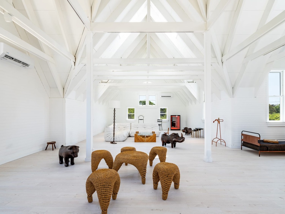 Bright spacious room with white beams, wicker elephant stools, modern furniture, and large windows.