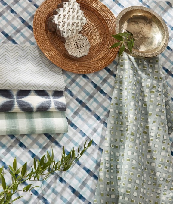 Assorted textiles and decorative items arranged on a blue plaid background with greenery for an elegant display.