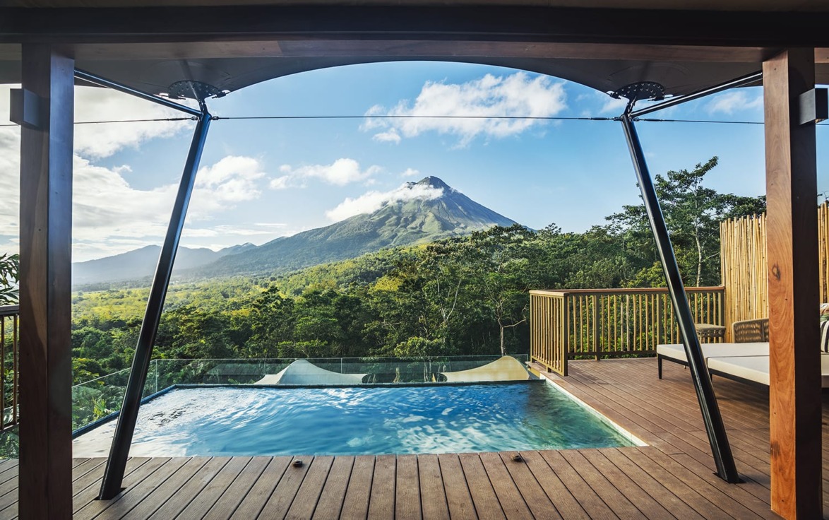Infinity pool with a breathtaking view of a lush green forest and a majestic mountain under a clear blue sky.