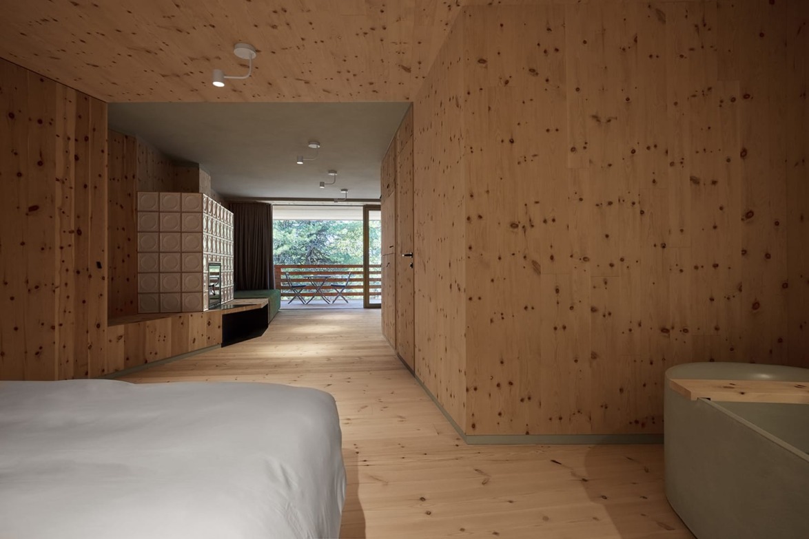 Minimalist wooden bedroom with a view of an outdoor balcony through large windows, featuring modern lighting and decor.